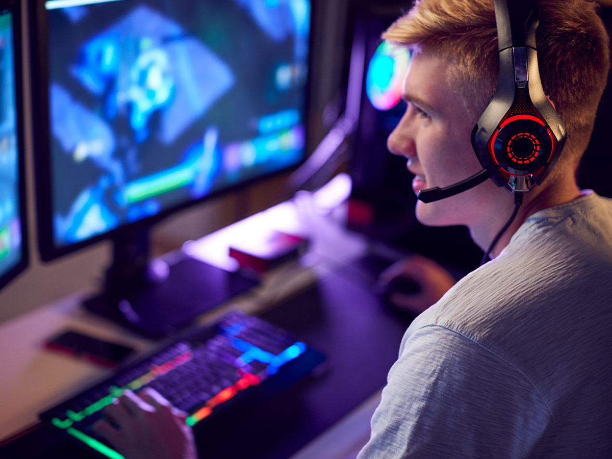 Image of a young man wearing a headset and playing a game using a  dual monitor